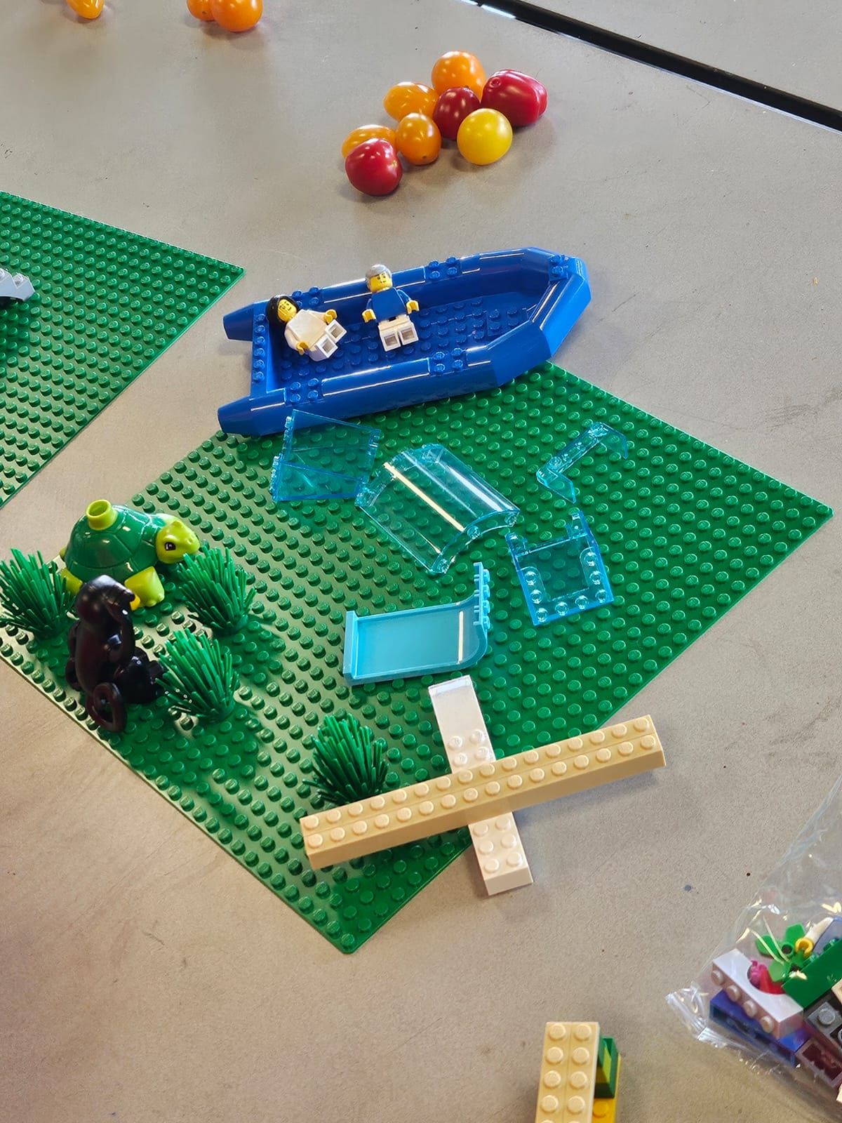 A LEGO model with a boat, figures and transparent pieces on a green base.
