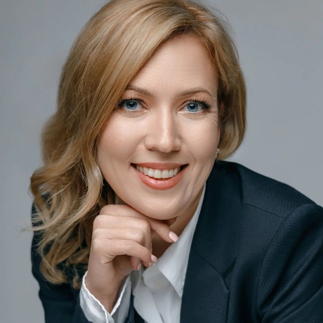 Portrait of Olga wearing a dark blazer and smiling at the camera.